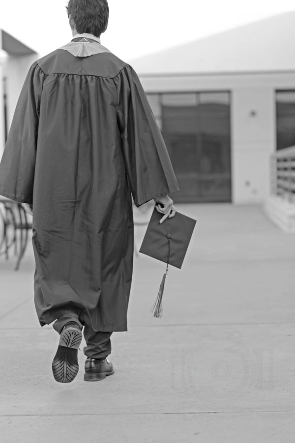 former high school student walking away from photographer during senior portrait session wearing diploma gown and barely holding cap in right hand tassel dangling olive branch ms