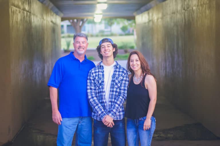 excited new high school graduate standing with loving parents in matching outfit with dad during senior photo services with danielle jacqueline