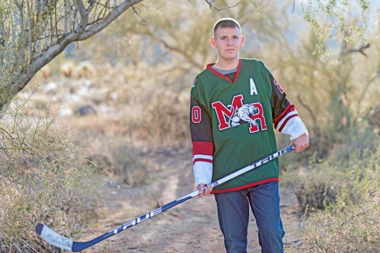 younf boy high school senior hockey playing standing outside in uniform holding stick for graduation portraits with danielle jacqueline now in olive branch ms