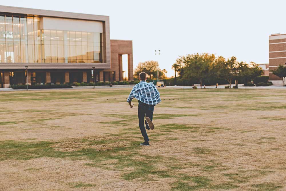 senior boy ideas running away from photographer in open field in front of school jeans and flannel for graduation celebration in olive branch ms