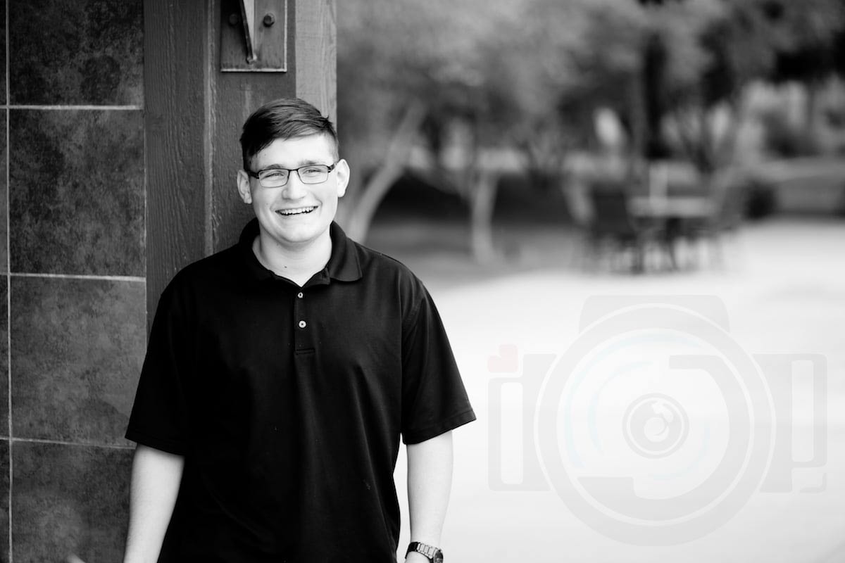 black and white photo of high school senior leaning against brick wall outside sports facility in desoto county ms with blank space for danielle jacqueline photography logo to the right big smile