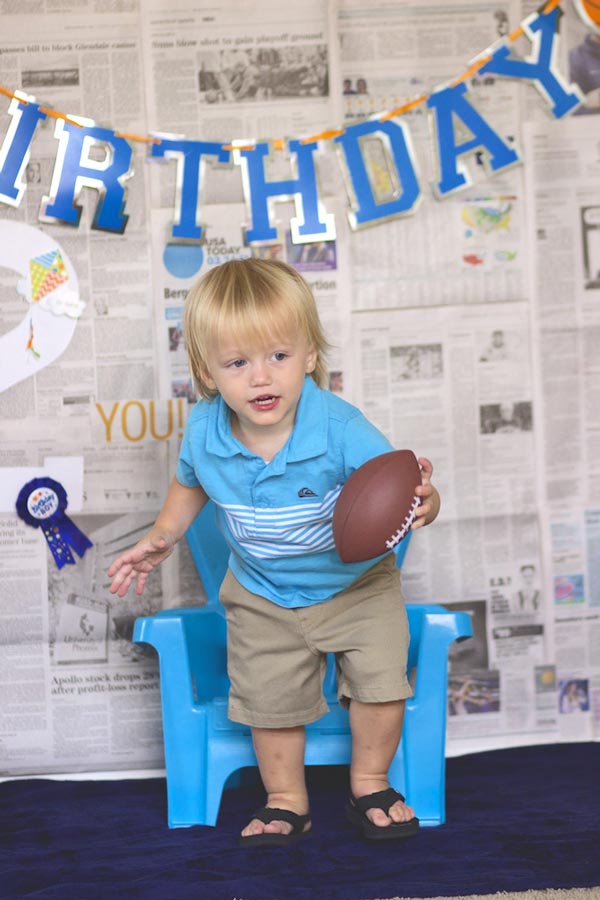 toddler escaping his baby chair with a little football in front of his birthday display by professional photographer studio in olive branch ms blue theme