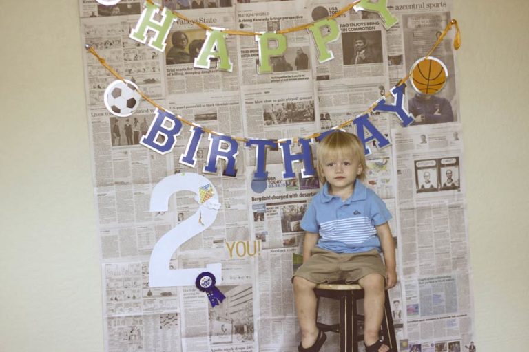 terrible twos photographer in olive branch mississippi capturing son on black stool in front of custom backdrop with newspaper dates and bday signage for blog