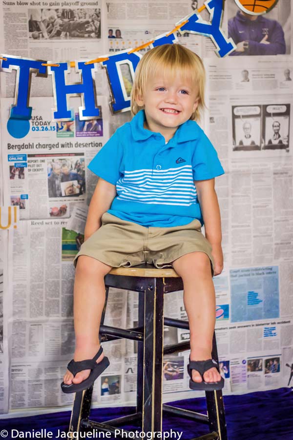 big smiling toddler boy on black stool in front of birthday theme settings by danielle jacqueline photography in olive branch ms