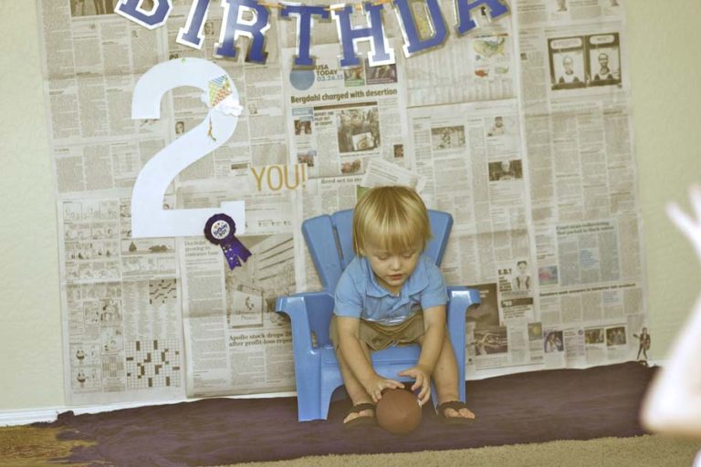 little boy seated on blue chair in front of diy photography display created at home by parents of toddler in olive branch mississippi