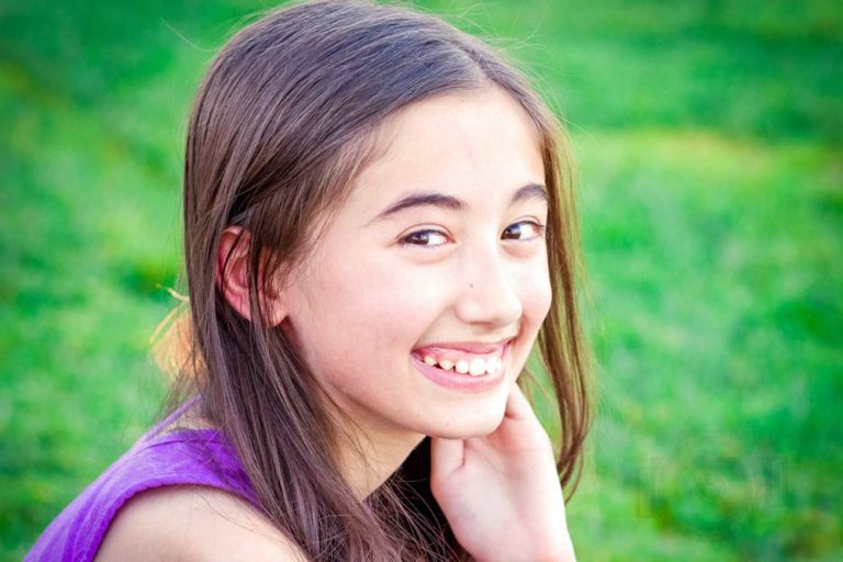 bright green grass background big gum smile by young girl with hand placed behind ear turning naturally toward camera to capture child's personality by danielle jacqueline photography near germantown tennessee