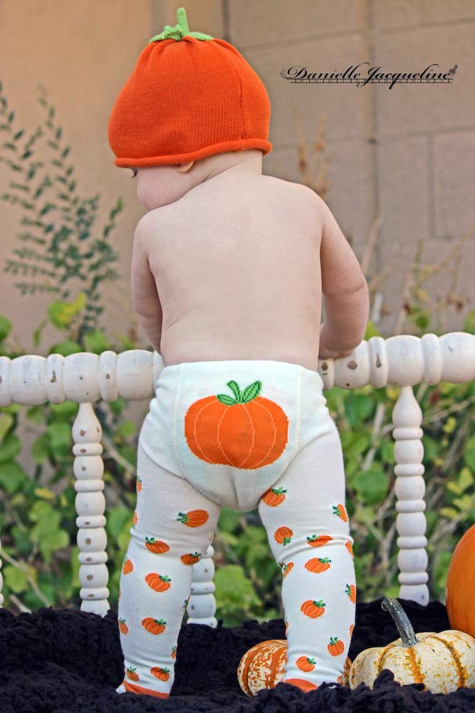 diaper wearing crawler holding self up white bench in backyard during fall photography session with danielle jacqueline with pumpkins and orange and brown theme in oxford ms