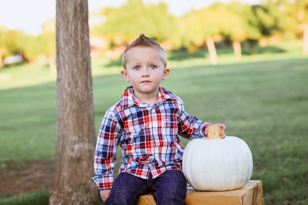 little boy sitting outside during family portrait session with white pumpkin blue eyes looking at camera confused for fall portraits in desoto county ms