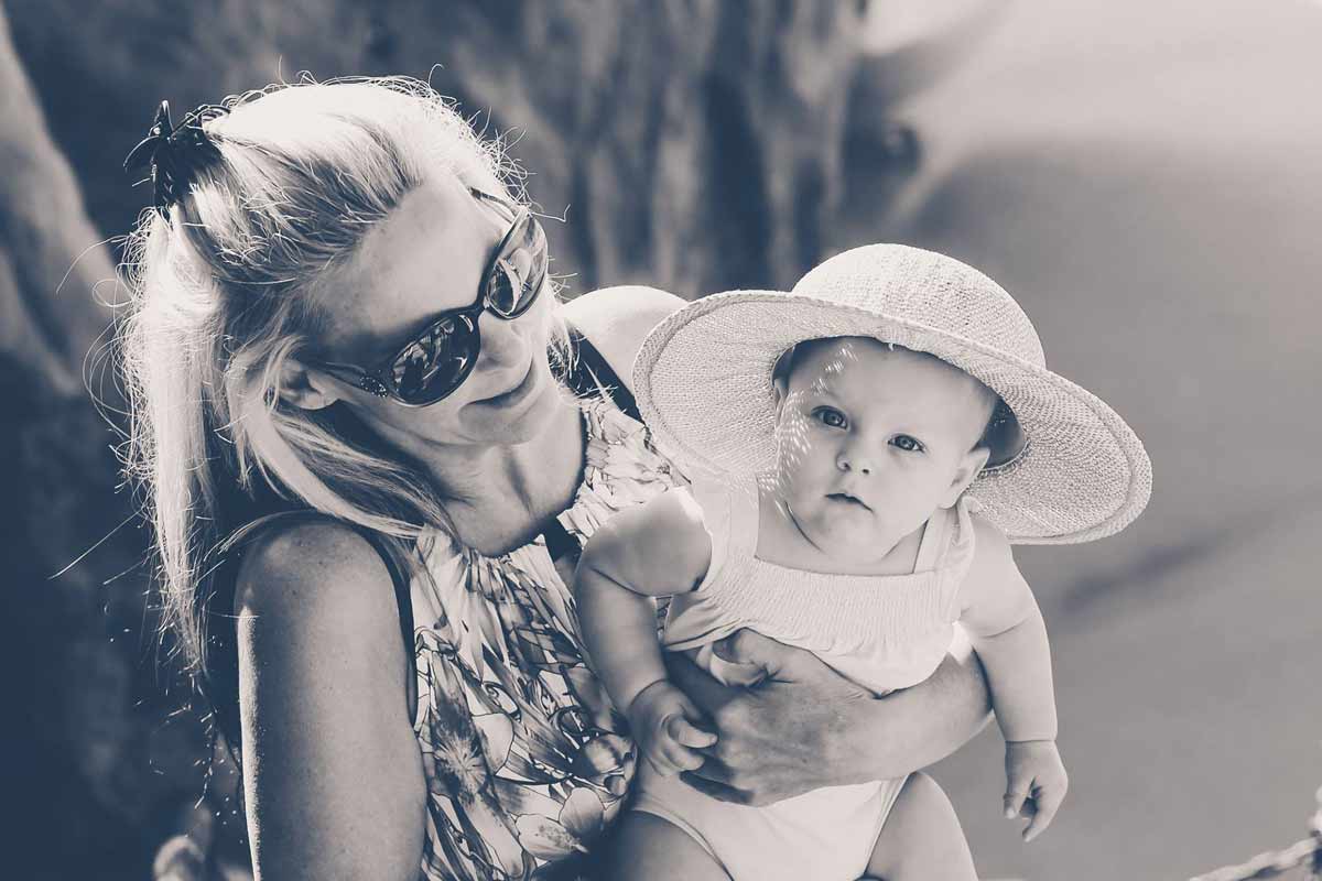 grandmother in shades holding baby girl looking directly at camera wearing sunhat during summer photo session in olive branch ms by danielle jacqueline