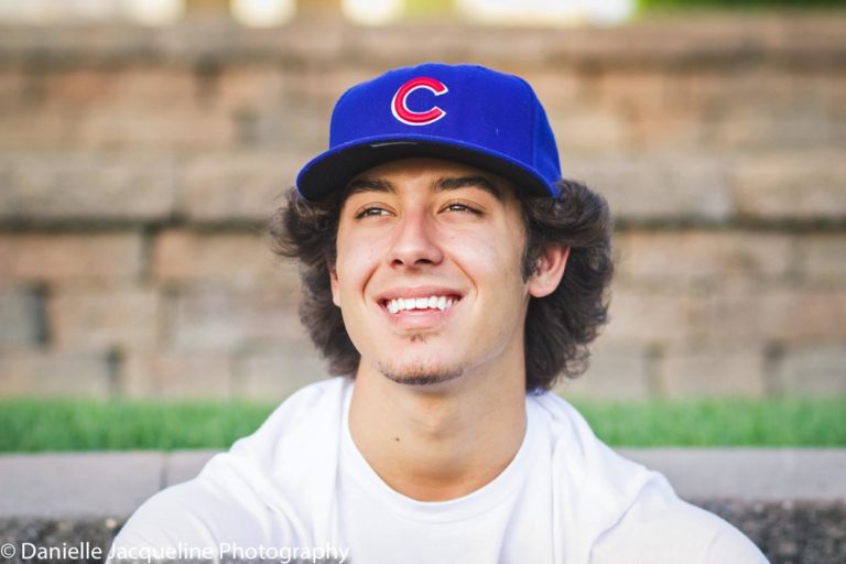 good smile minor squint under bill of cubs hat white tee in front of grass and stone steps at park with danielle jacqueline photography in desoto county ms