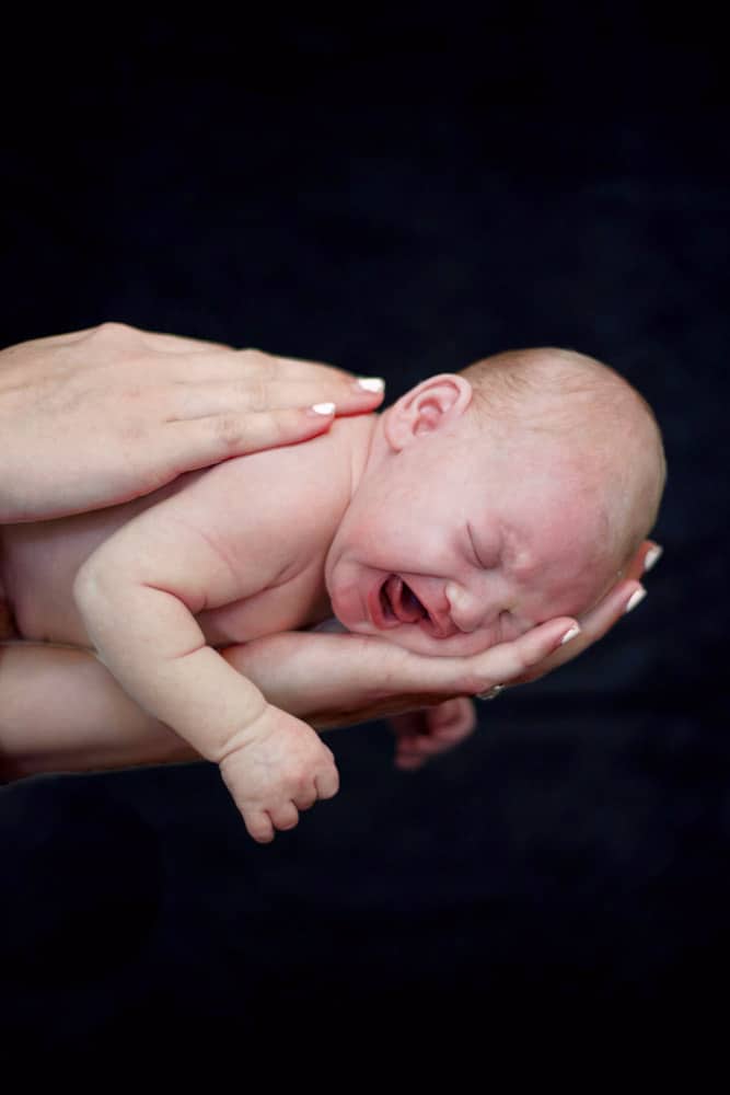 amazing newborn baby photography of mother holding fresh born son in hands as he cries skin color black background candid moment for parents near memphis tennessee looking for unique studio sessions