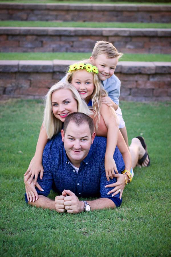 dad on the bottom of a pile in the grass facing camera with wife on his back then daughter and son to form family pyramid for summertime portraits for families with danielle jacqueline photography in midsouth mississippi