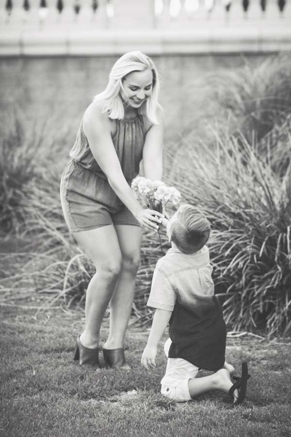 mom in jean outfit slightly bending down to grab picked flowers from little boy in grass during family photo shoot by danielle jacqueline near memphis tn