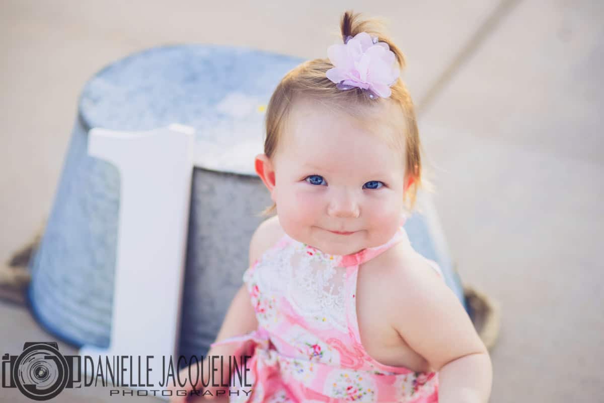 little girl with bow in her hair and pink dress in front of aluminum trough upside down on side walk for birthday pictures with danielle jacqueline outside desoto county ms