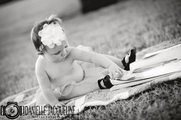 angled photograph black and white of little girl playing in dress shoes and tutu for first birthday pictures in memphis tn with danielle jacqueline outside during spring