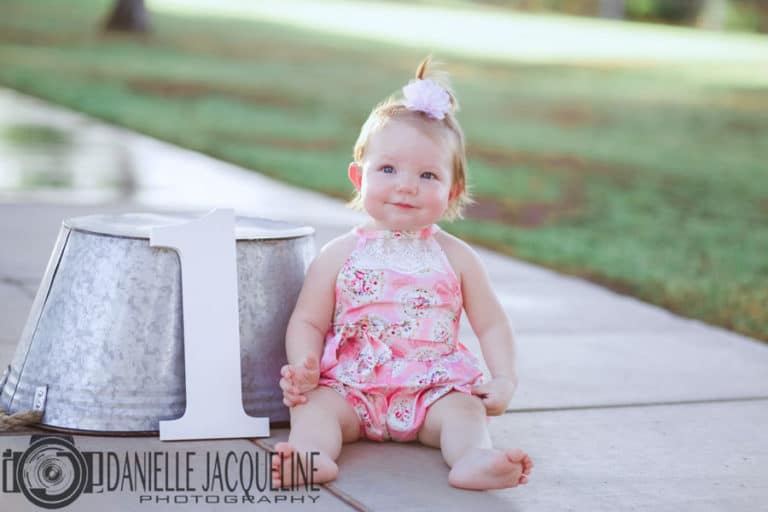 perfectly situated 1 year old baby girl next to metal trough and painted white #1 outside for birthday pictures with danielle jacqueline out of olive branch ms