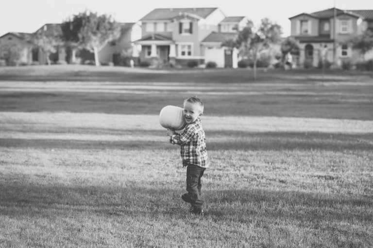 little boy carrying painted pumpkin in middle of residential park in suburban setting outside memphis tennessee for fall family pictures with danielle jacqueline black and white edit