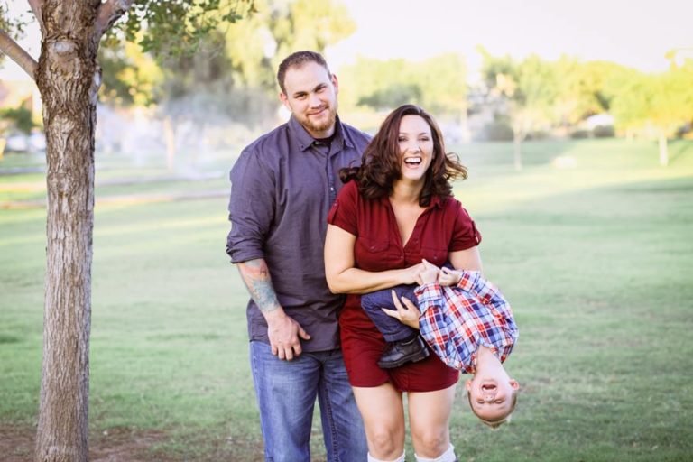 little boy flipping back while mommy is holding him laughing out of control with dad looking as if he's enjoying himself in front of open grass field at desoto county park by danielle jacqueline photography