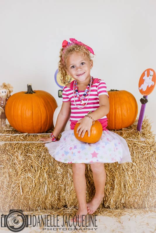 happy little lady on bails of hay next to pumpkins and fall signage with props on october 31st 2016 diy photo studio lighting project