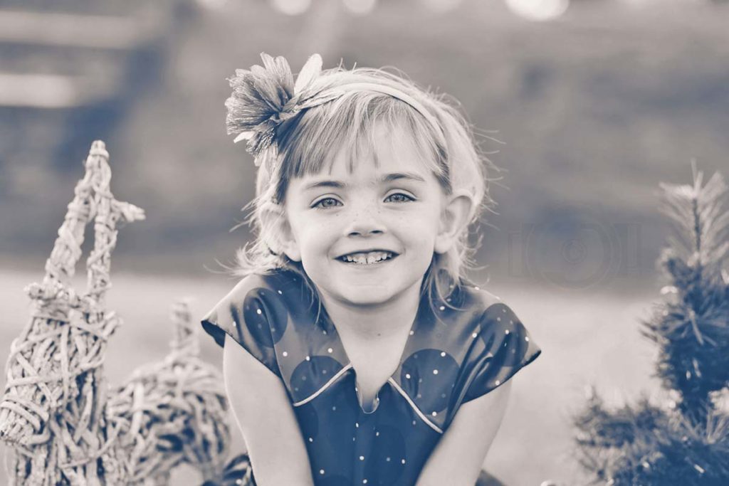 little girl beat cancer with family for winter holiday pictures outside with danielle jacqueline photography in olive branch ms with small christmas tree and other props bow in hair pretty dress black and white