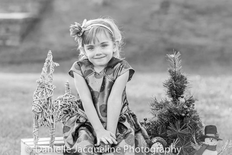 shoulders up comfortable looking at photographer innocently with parents during family winter photoshoot with danielle jacqueline outdoors christmas props