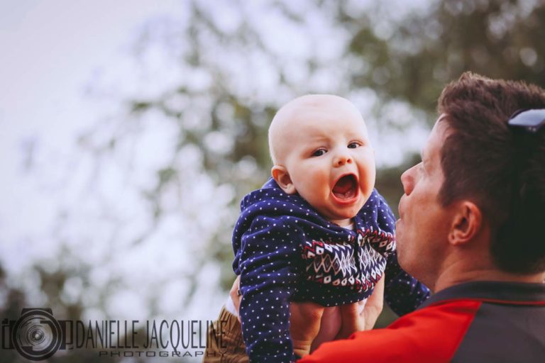 young son being raised into the air by his father with trees above junior portraits captured from below behind shoulder by danielle jacqueline photography in olive branch ms