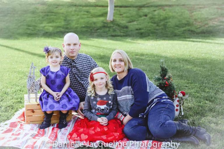 family of four sitting on christmas quilt in the middle of park on grass for winter holiday portraits by danielle jacqueline located in olive branch ms