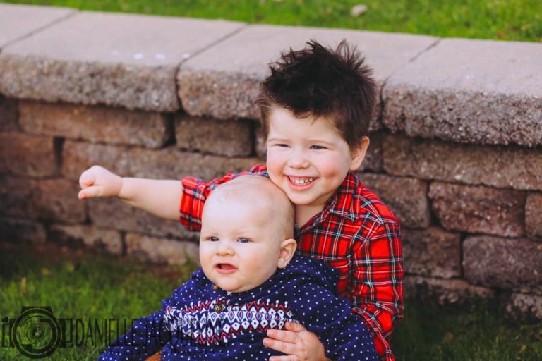 christmas sweater wearing little boys leaning against rock steps in grass at olive branch mississippi park for junior portraits with danielle jacqueline photography