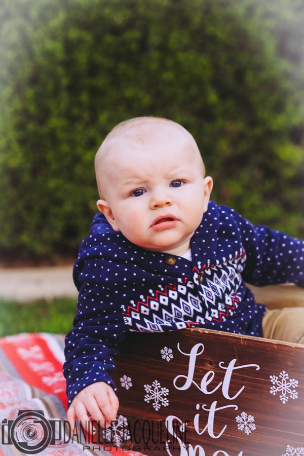 what are you looking at baby seated in christmas themed box on top of holiday colored red blanket with white snowflakes knitted on it and douglas fur in background for pictures with danielle jacqueline in olive branch ms