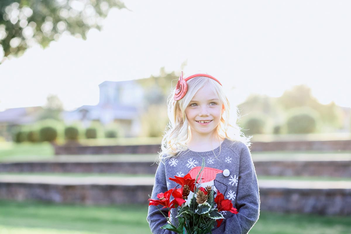 young lady photogenic for winter family photo session next to stone stairs at park wearing holiday attire