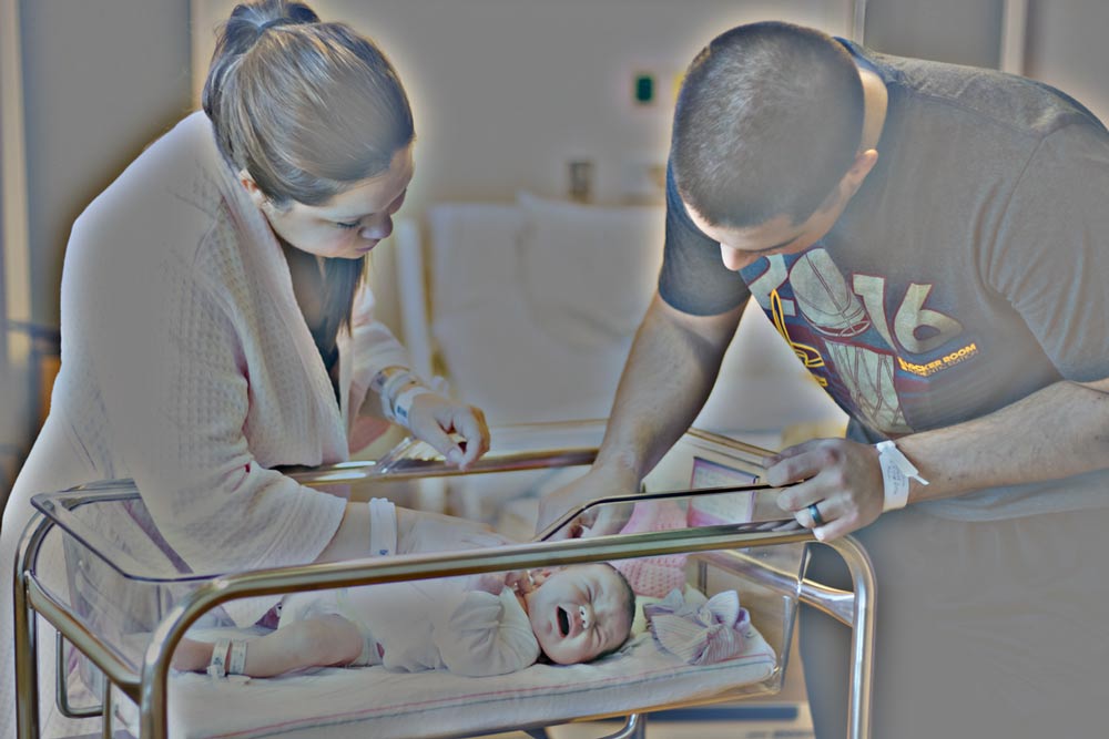 new parents both reaching down to care for crying infant in recovery room at hospital during fresh 48 session with danielle jacqueline photography near memphis tennessee