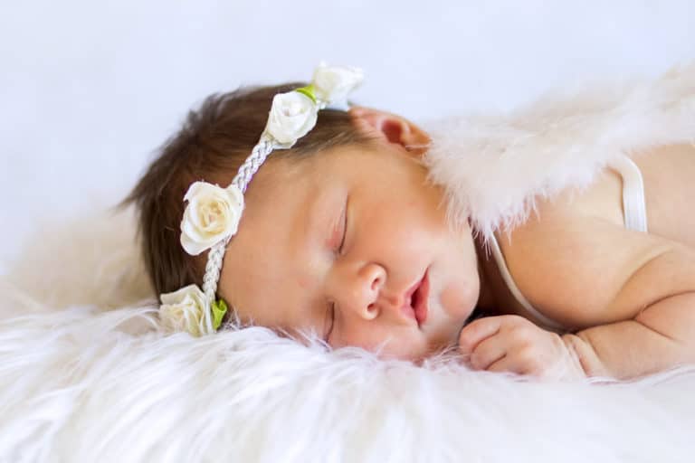 white headband with flowers on it sleeping infant new arrival girl laying on tummy eyes closed dreaming with prop angel wings on back at danielle jacqueline photography studio now located in olive branch ms