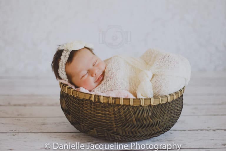 cute little smirk by sweet little baby girl in woven wicker basket and white background at danielle jacqueline photography studio in olive branch ms