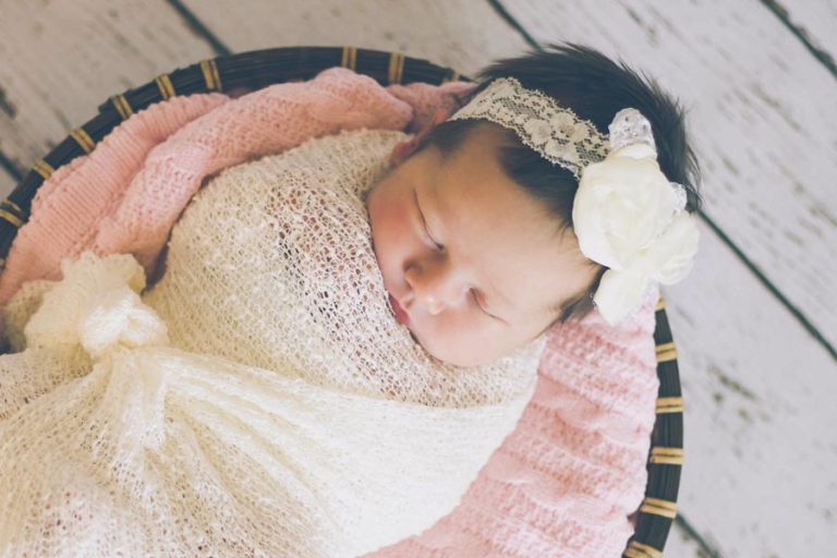 cozy baby angel girl swaddled inside pink draped basket with vinyl white wood backdrop for infant photography session with danielle jacqueline south of memphis tennessee