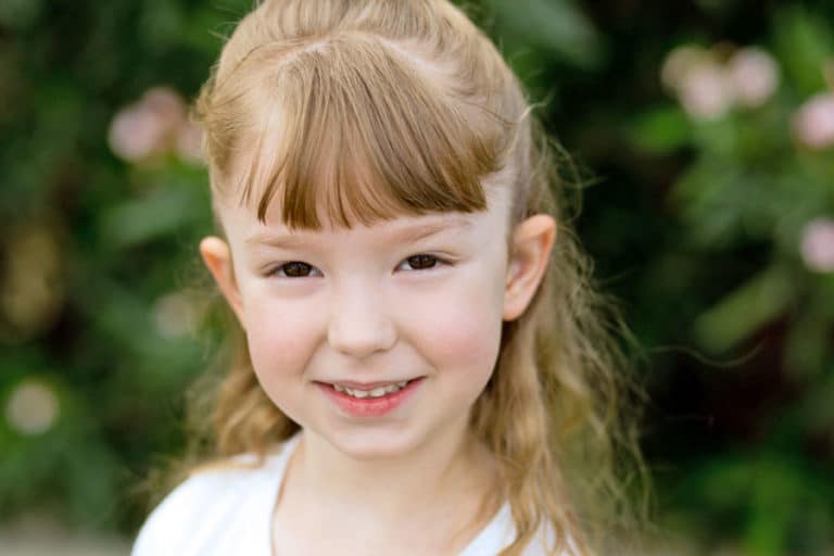 cute close up portrait of strawberry blonde preschooler in white shirt with flowers blooming in background captured by danielle jacqueline photography in south memphis tennessee stateline