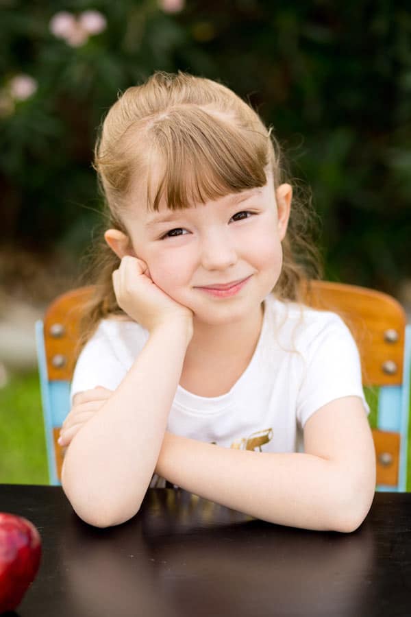 angel soft portrait outdoors for preschool girl pose with arm to cheek situated at desk with red apple for teacher adorable by danielle jacqueline photography in olive branch mississippi