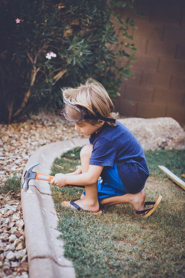 concrete backyard grass boundary being hit with hammer by 4 year old boy for photographer mom blog growing as new residents in olive branch ms