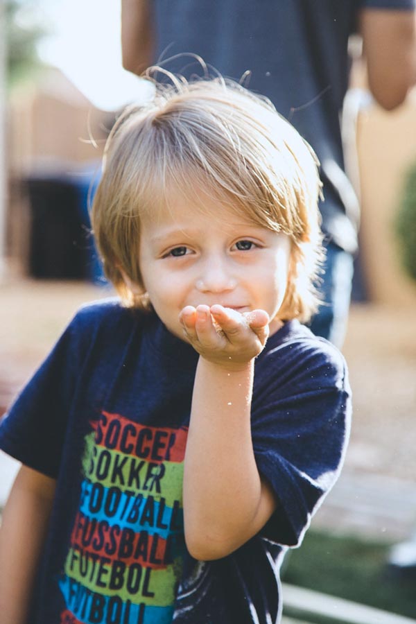 grinning 5 year old sun with sawdust in palm of hand getting ready to blow it at photographer's camera outdoors in mississippi