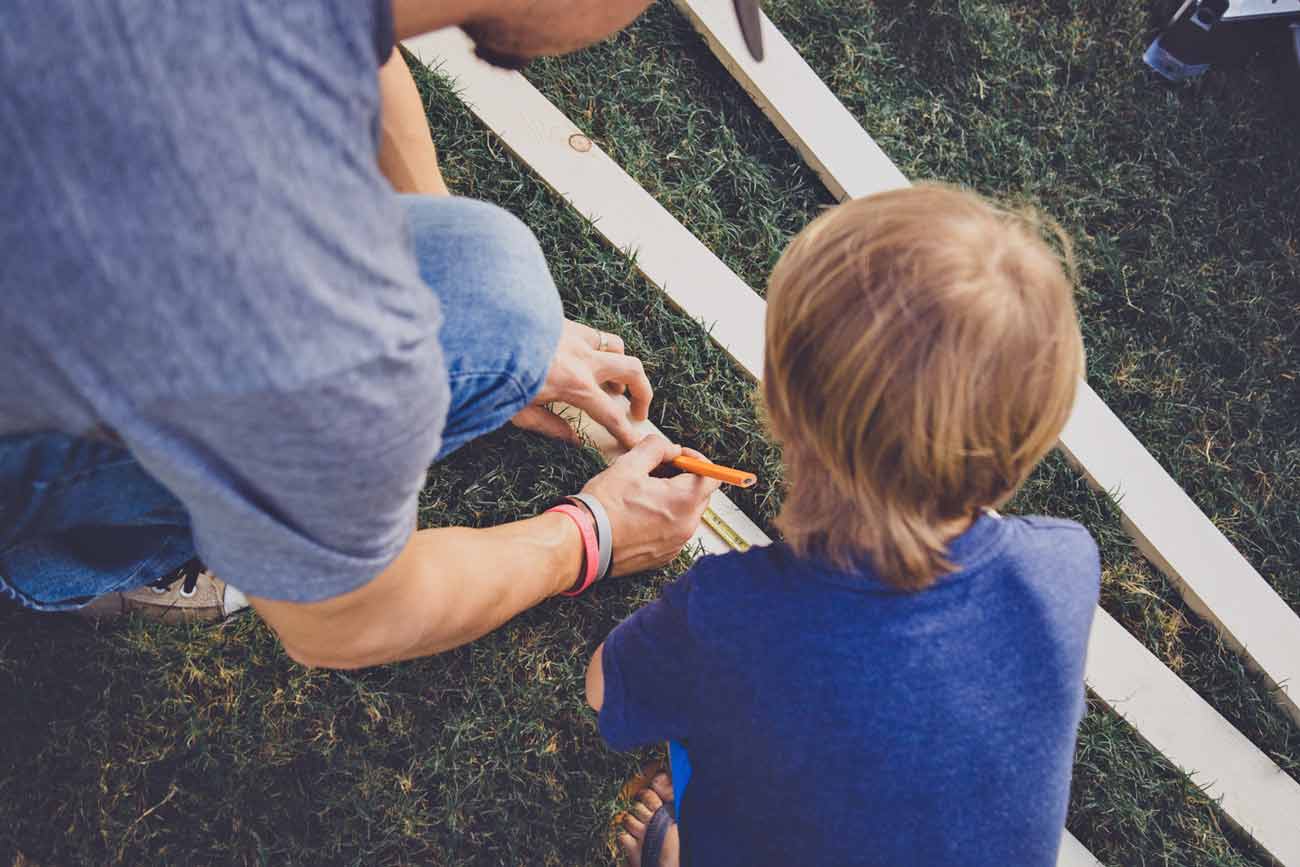 daddy using tape measurer before cutting 1x2 piece of lumber for bench repair during family time with the trasks in olive branch ms