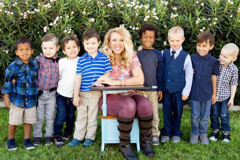 pre-kindergarten teacher sitting in small desk center of boy students for class picture outside in front of flowered bushes by danielle jacqueline photography in desoto county, mississippi