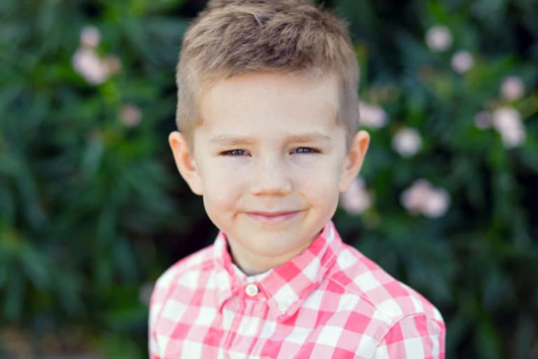 smiling young man red and white checkered shirt with bright green shrubs in background for children's preschool portraits by olive branch photographer danielle jacqueline in mississippi