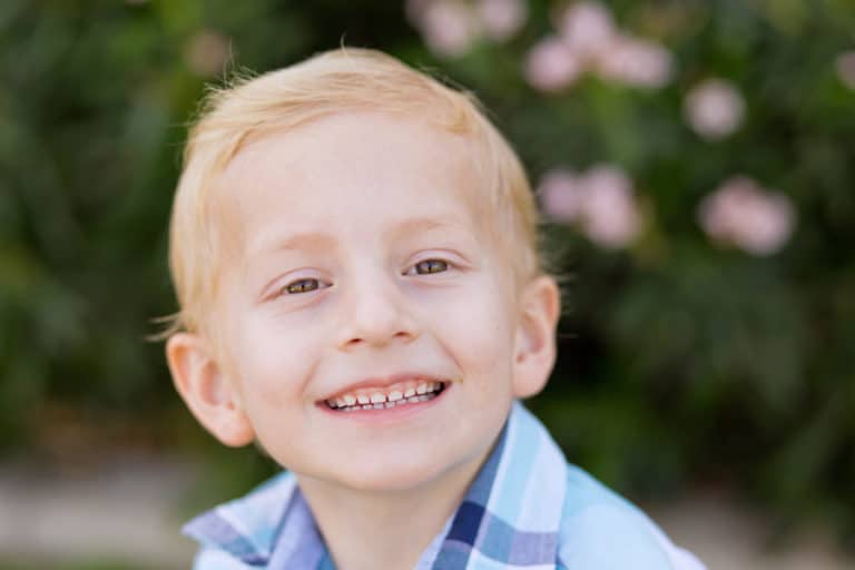 sideways grin by 6 year old boy for class pictures outside with pink flowers blurred in background with vegetation close ups by danielle jacqueline in southern memphis tennessee