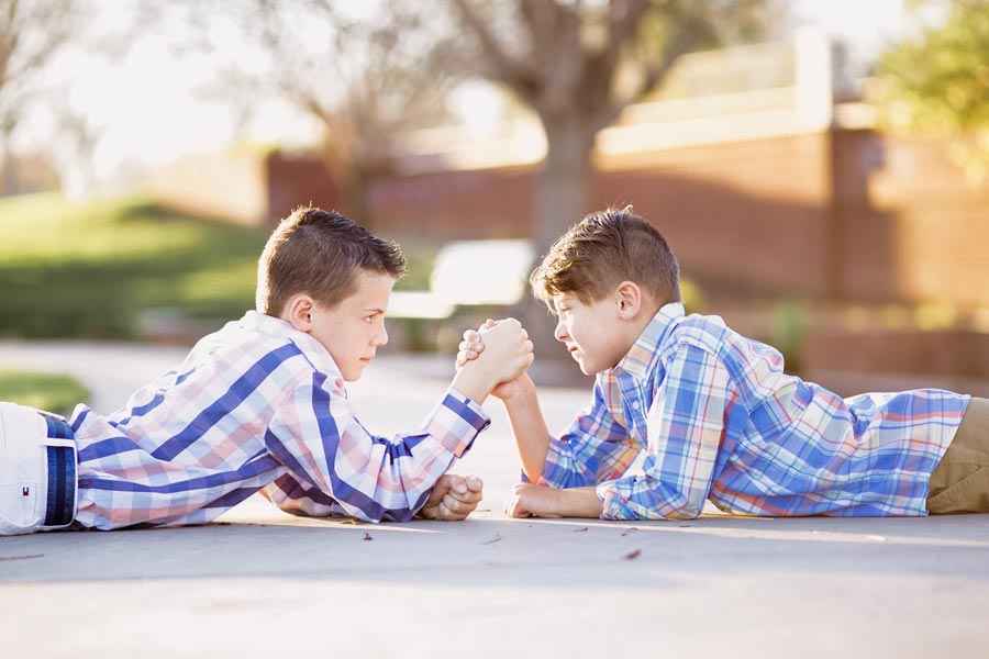 two competitive brothers close in age arm wresting on pavement at park dressed formally for family portraits depicting sibling rivalry candid moment by danielle jacqueline photography near germantown tn