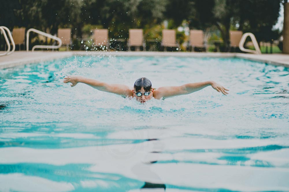 butterfly swimmer coming towards camera in large outdoor pool with lawn chairs in background splashes of water googles on from distance danielle jacqueline olive branch ms