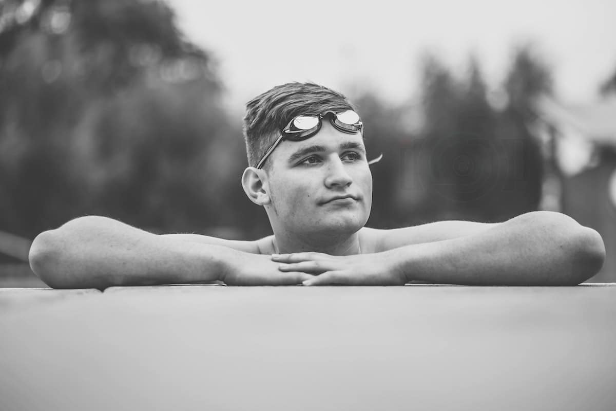 close up hero image of high school senior at edge of swimming pool for graduation session for athletes near memphis tenn black and white looking right arms folded on deck eye level