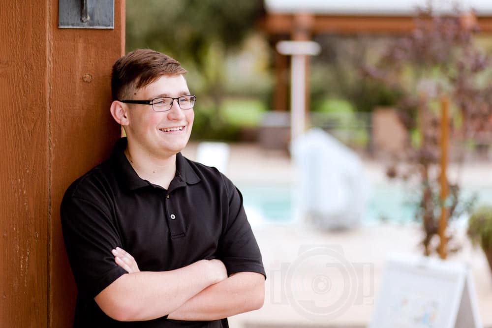 formal student athlete poses with sport reference in background black polo arms crossed glasses smiling in front of pool for graduation by danielle jacqueline olive branch ms