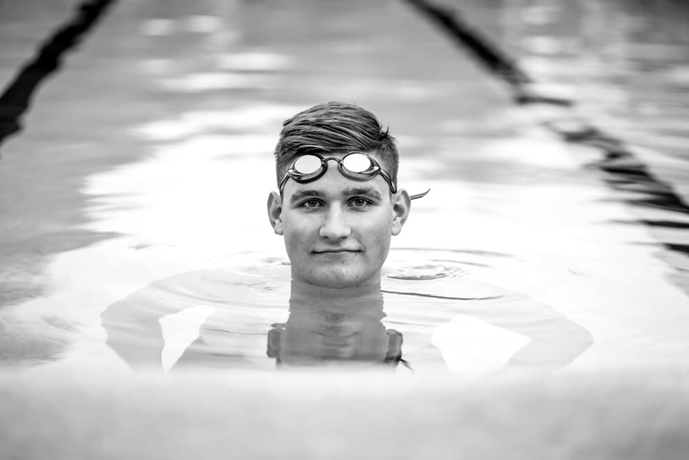 center of attention in swimming pool 5 ft water level black and white high school senior portrait goggles on forehead athletic theme near memphis tn