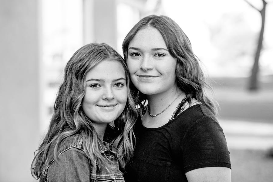 two sisters smiling during family event outdoors teenagers without parents by danielle jacqueline black and white photography in olive branch ms