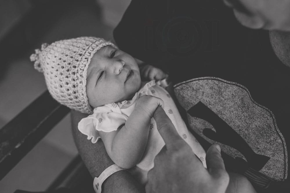 newly born little girl holding first time daddy's finger during close up shot in his arms looking into his eyes black and white beanie soo cute by danielle jacqueline photography near memphis tennessee