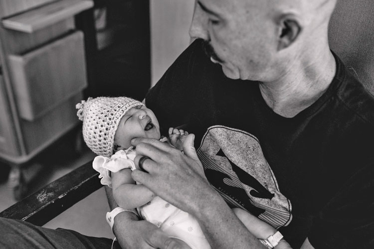 baby daughter crying in father's hands black and white photo trying to soothe her in arms stinky diaper hospital portrait memphis tn